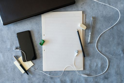 A top view of a blank sheet with smartphone, earphones, pen, pencil, eraser and sharpener