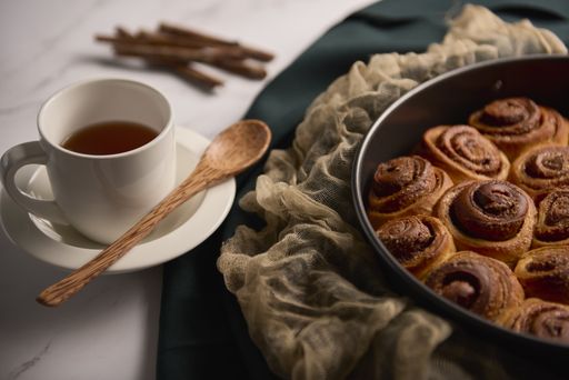 A high angle shot of freshly baked cinnamon roll buns with a wooden spoon, tea, and cinnamon