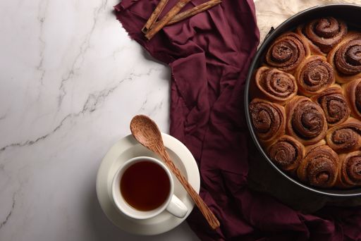A high angle shot of freshly baked cinnamon roll buns with a wooden spoon, cinnamon, and tea