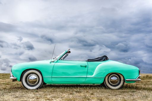 A closeup shot of a green car parked on a dry field under a cloudy sky