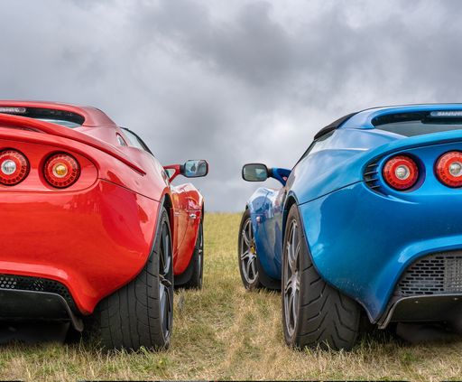 A closeup shot of red and blue cars next to each other under a cloudy sky