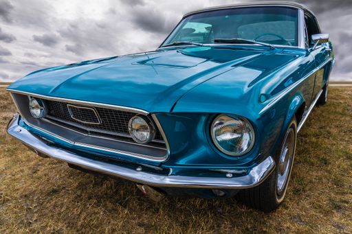 A closeup shot of a blue car parked on a dry field under a cloudy sky
