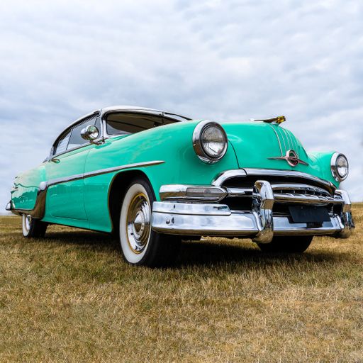 A closeup shot of a turquoise vehicle on a dry field under a cloudy sky