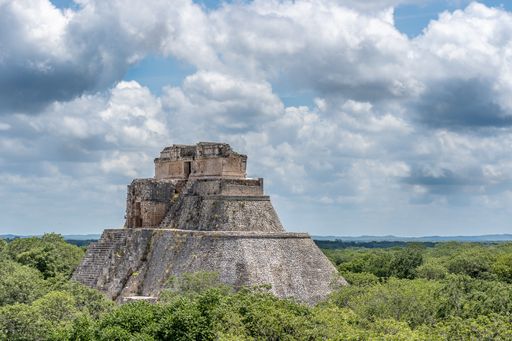 A wide angle shot of the Pyramid of the Magician in Mexico surrounded by trees under the blue sky