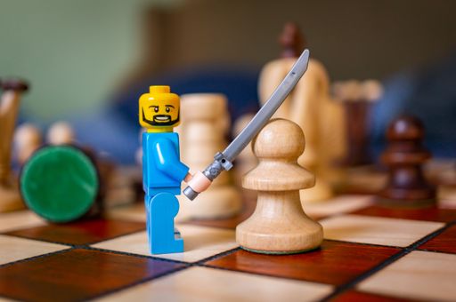 Lego man toy figurine holding up a sword in front of a chess piece on a board.