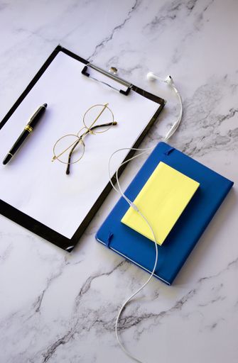 A top view of a notepad with a to-do list with glasses and a pen on a marble surface