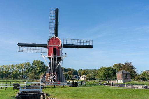 A windmill under a clear blue sky surrounded by trees and vegetation