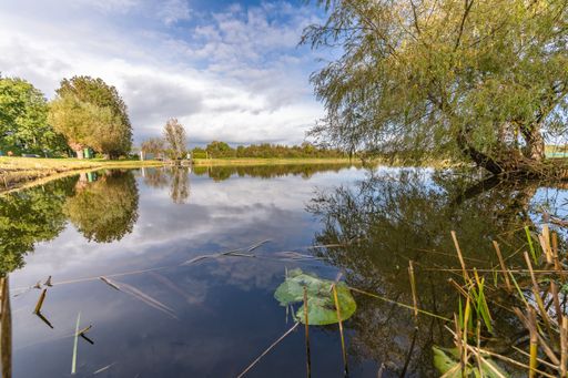 A wide angle shot of the water surrounded by trees and green landscapes under a clear blue sky