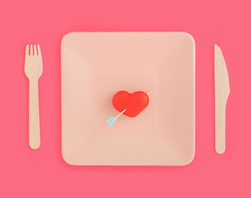 A top view of a red heart-shaped macaron with an arrow on a plate with a fork and knife on the tabl