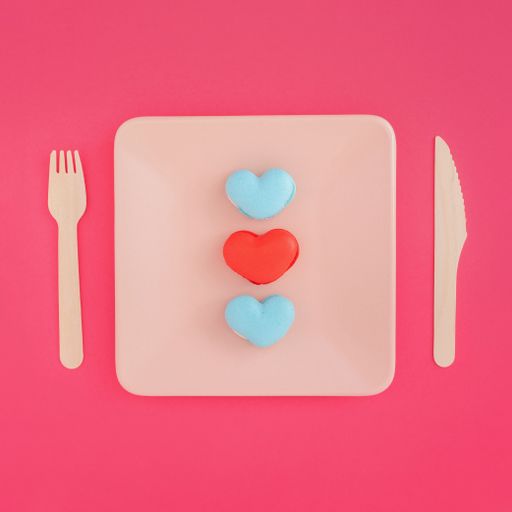 A top view of heart-shaped macarons with an arrow on a plate with a fork and knife on the table