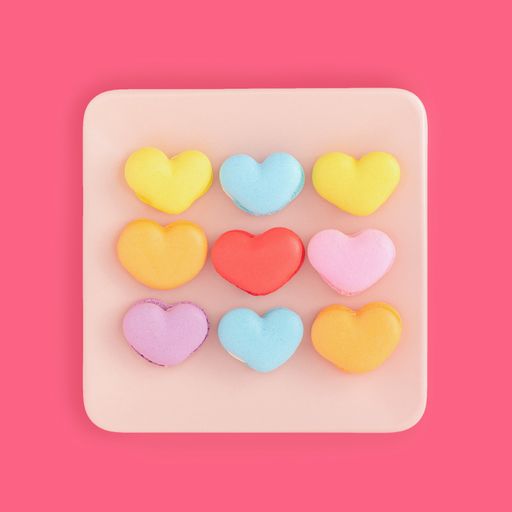 A top view of colorful heart-shaped macarons on a plate on a pink surface