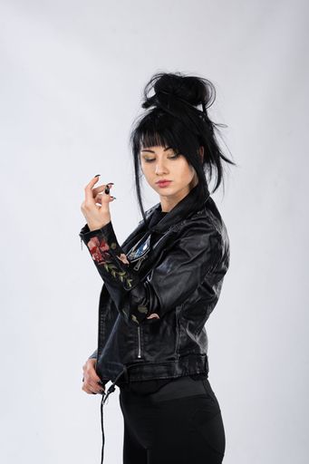 A caucasian woman in leather clothes posing against the white studio wall