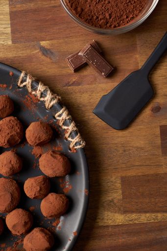 A vertical top view of chocolate truffles on a table with ingredients in the background