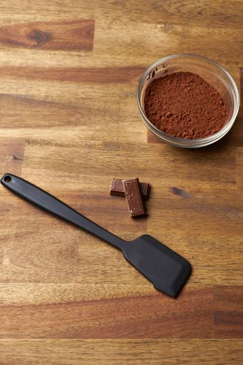 A top view of cocoa powder and a kitchen shovel on a wooden surface