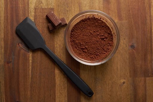 A top view of cocoa powder and a kitchen shovel on a wooden surface