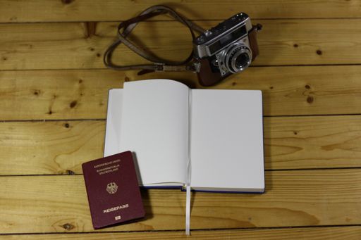 A high angle shot of an open notebook next to a passport and a camera on a wooden surface