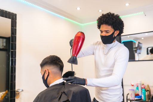 A male hairdresser with a mask cutting the hair of a young man