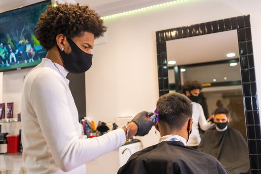 A Latin hairdresser with a protective mask and gloves cutting the client's hair with a razor