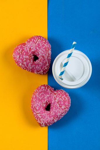 A vertical top view of heart-shaped donuts and a cup of coffee on a colorful background