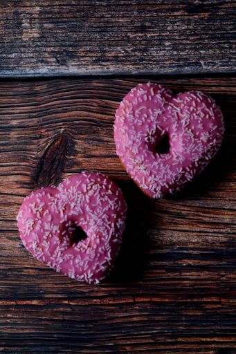 A vertical top view of two heart-shaped donuts with sprinkles