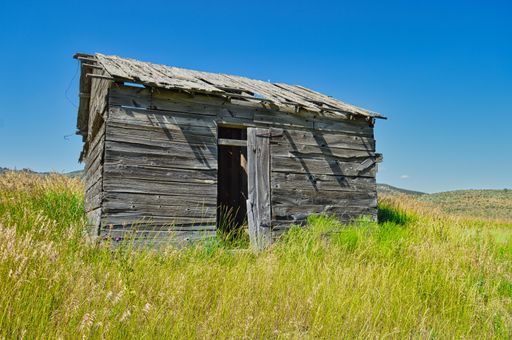 An old wooden barn in the middle of a field under a bright sky