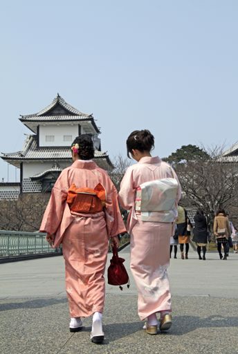A vertical shot of two women walking towards the Kanazawa Castle Park in Japan