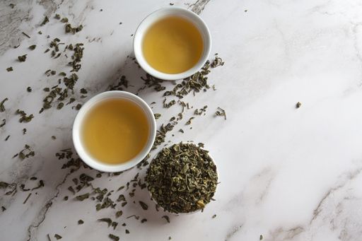 A closeup of green leaf tea and two containers on marble background