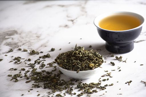 A selective focus shot of green leaf tea and a container on marble background