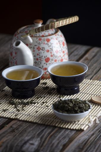 A vertical selective focus shot of green leaf tea, two containers and kettle on wooden background