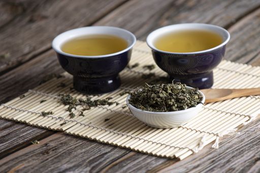 A selective focus shot of green leaf tea and two containers on wooden background