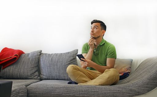 A man sitting on a sofa behind a white wall thinking about something