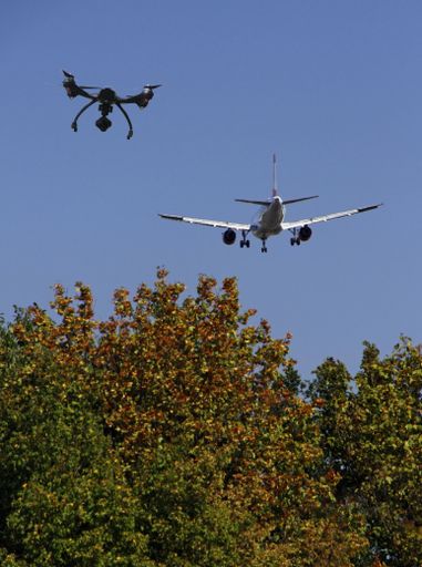 A low angle shot of a drone and an airplane flying next to each other over the trees