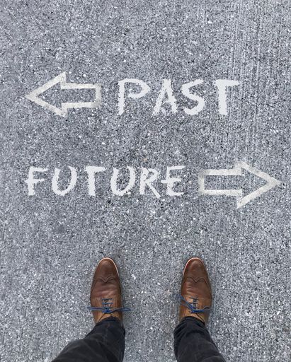 A vertical shot of the words Past Future and arrows written on the ground in front of a man's shoes