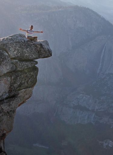 A vertical shot of a man sitting on a stone in front of the mountains in Yosemite National Park