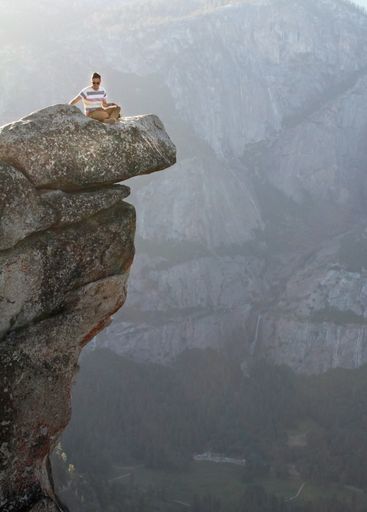 A vertical shot of a man sitting on a stone in front of the mountains in Yosemite National Park