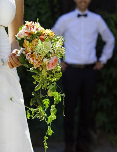 A vertical shot of a man standing behind the bride holding flowers in her hands