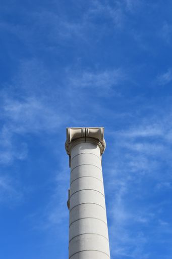 A low angle shot of a white lonic style stone column against a blue sky