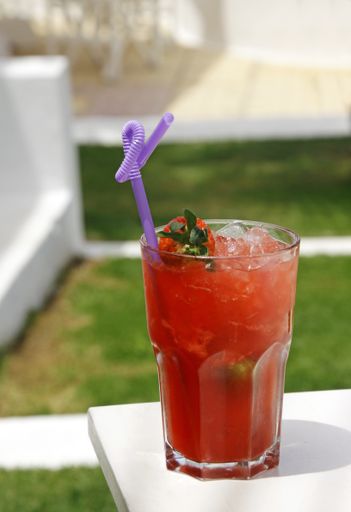 A vertical shot of a red cocktail with a purple straw under the sun