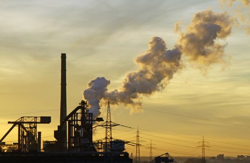 A wide angle shot of smoke coming out of factories surrounded by electricity towers during a sunset