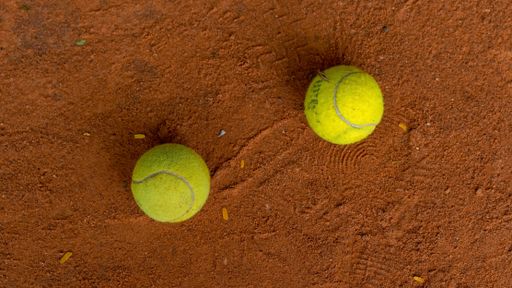 Two tennis balls on the orange ground in a tennis court