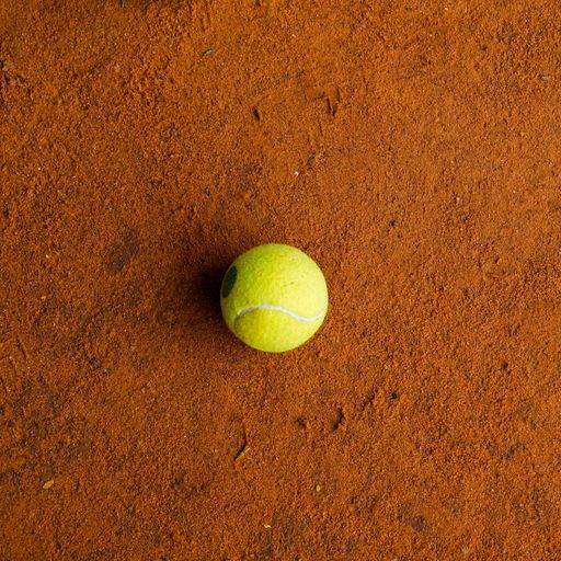 A tennis ball on the orange ground in a tennis court