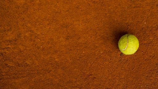 A tennis ball on the orange ground in a tennis court