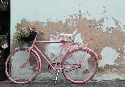 A wide angle shot of a pink bicycle next to an old and damaged white wall