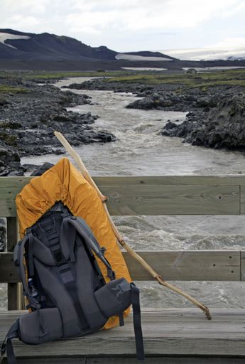 A vertical shot of a backpack behind a river during daytime