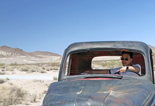 A wide angle shot of a man sitting in an old car on the desert