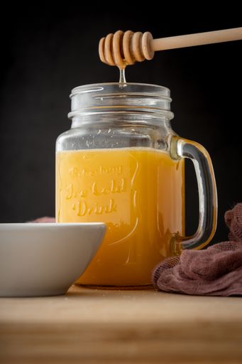 The process of adding honey into orange juice in a beverage mason container on a wooden table