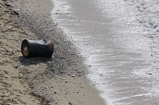 A large metal container tossed on the sand of the beach