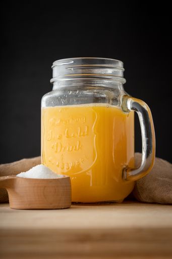 A small amount of sugar and beverage mason container filled with orange juice on a wooden table