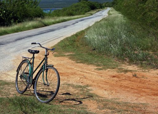 A white angle shot of a bicycle parked next to a road surrounded by grass and trees