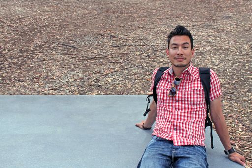 A wide angle shot of a man sitting on a stone surface surrounded by trees and leaves